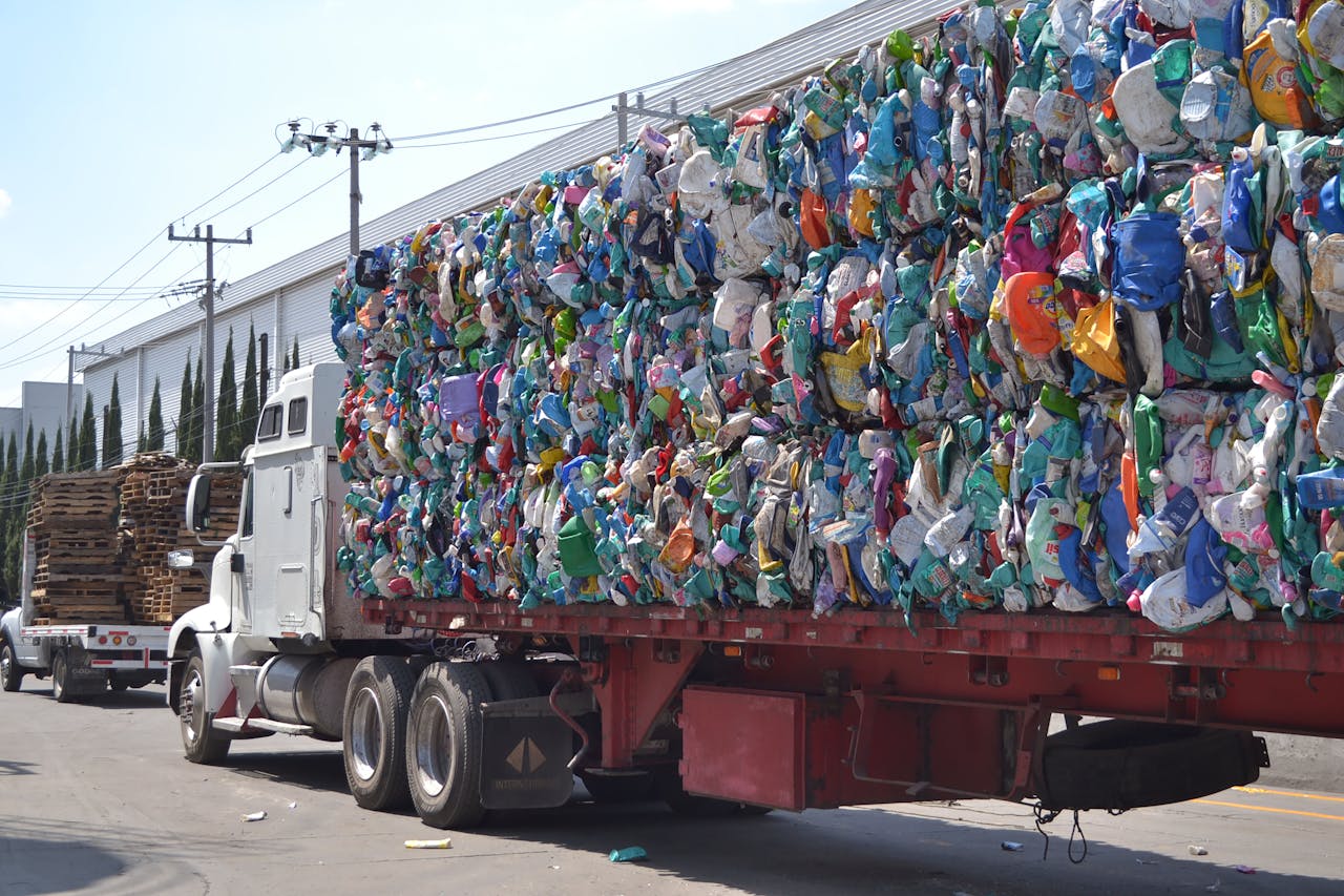A large truck carrying bales of compressed plastic waste on a sunny city street in Mexico.