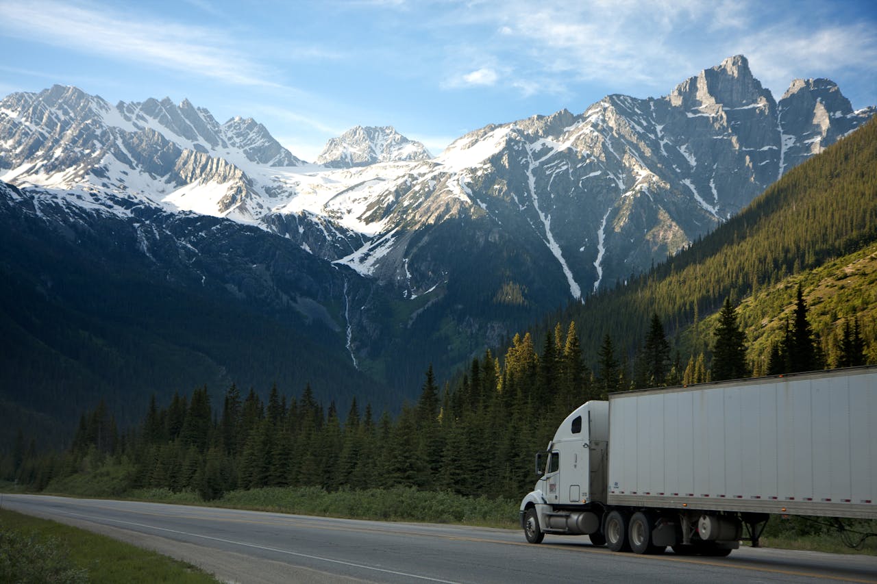 Services-02 A semi-truck travels along a highway with snow-capped mountains in the background.