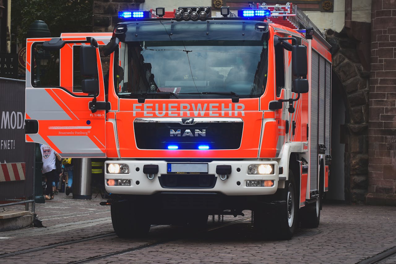 Bright red fire truck with blue lights on a city street in daylight.